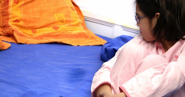 Niña mirando una mancha de pis en la cama