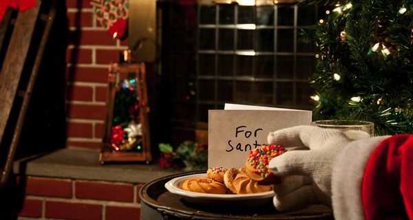 Papá Noel comiéndose las galletas que le han dejado junto al árbol de Navidad y la chimenea