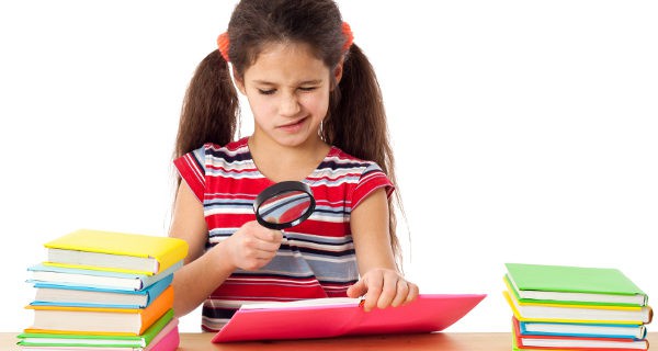 Niña mirando un libro con una lupa