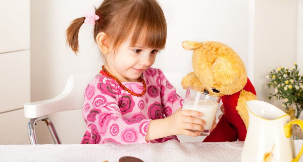 niña compartiendo su leche con un muñeco